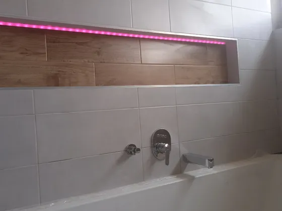 Hotová nika nad vanou s LED osvětlením a dřevodekorem.