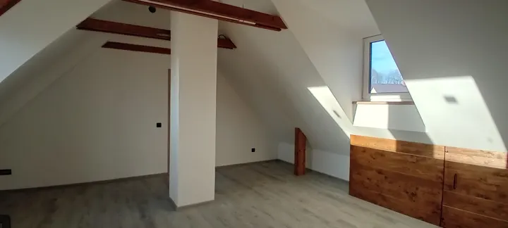 Podkrovní prostor s přiznanými dřevěnými trámy.