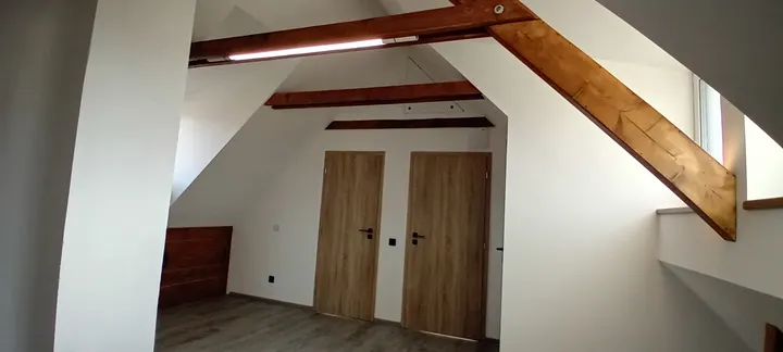 Dokončené podkroví s dřevěnými trámy a dveřmi.