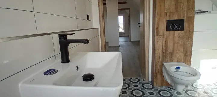 Koupelna s umyvadlem, WC a kombinací bílého obkladu a dřeva.