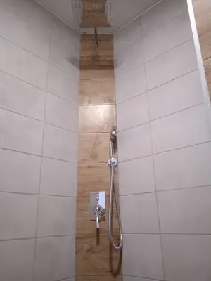 Dokončený sprchový kout se sprchovou sestavou a kombinací světlých obkladů s dekorem dřeva.